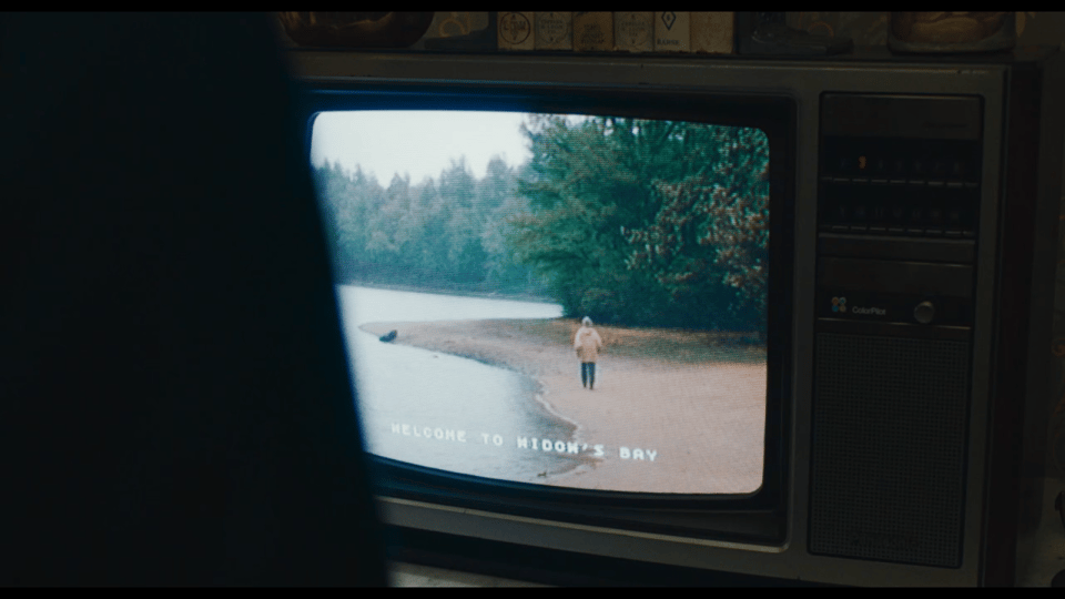 An old-fashioned tv showing the edge of a lake with a man walking away from the camera. The screen has "Welcome to Widow's Bay" across the bottom.