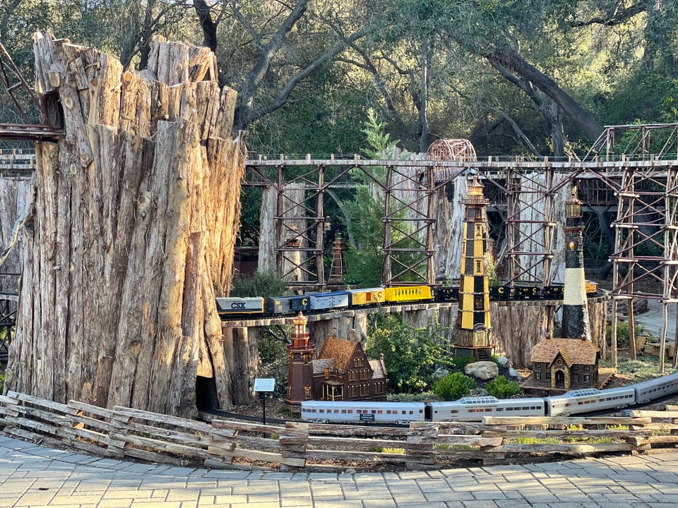 A large model train display. Multiple tracks weave between trees and wooden sculptures