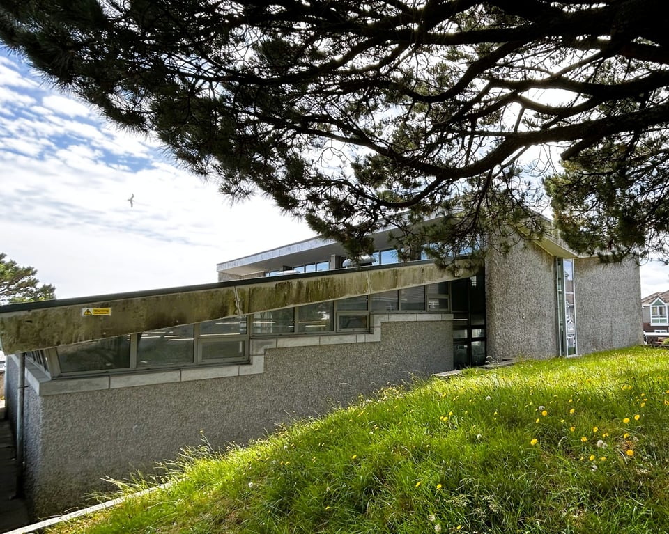 A pent roof extension connected to where the eastern curtain wall once was. The extension has rough cast concrete walls and stepped clerestory windows. And anti-climb paint and tar roof.