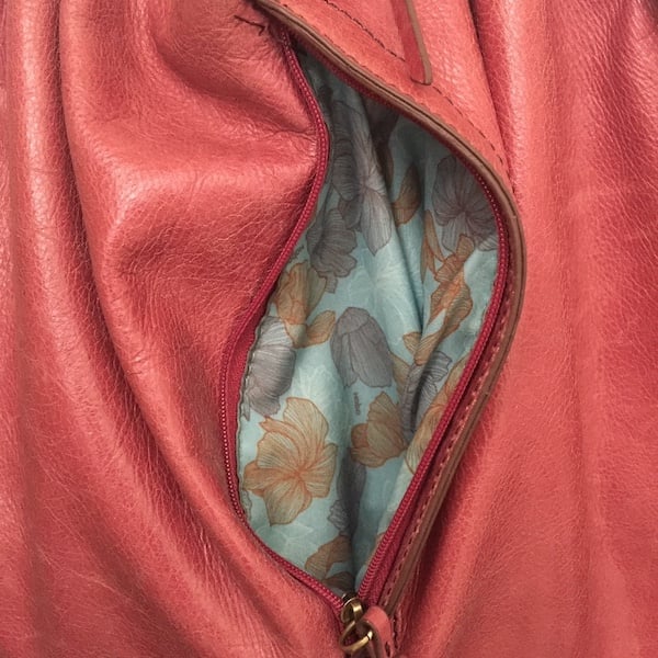 a red purse is unzipped revealing the floral fabric interior