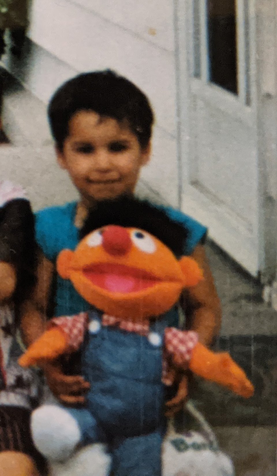 Derek as a young child, sitting down with an Ernie (Sesame Street) plush toy on his lap.
