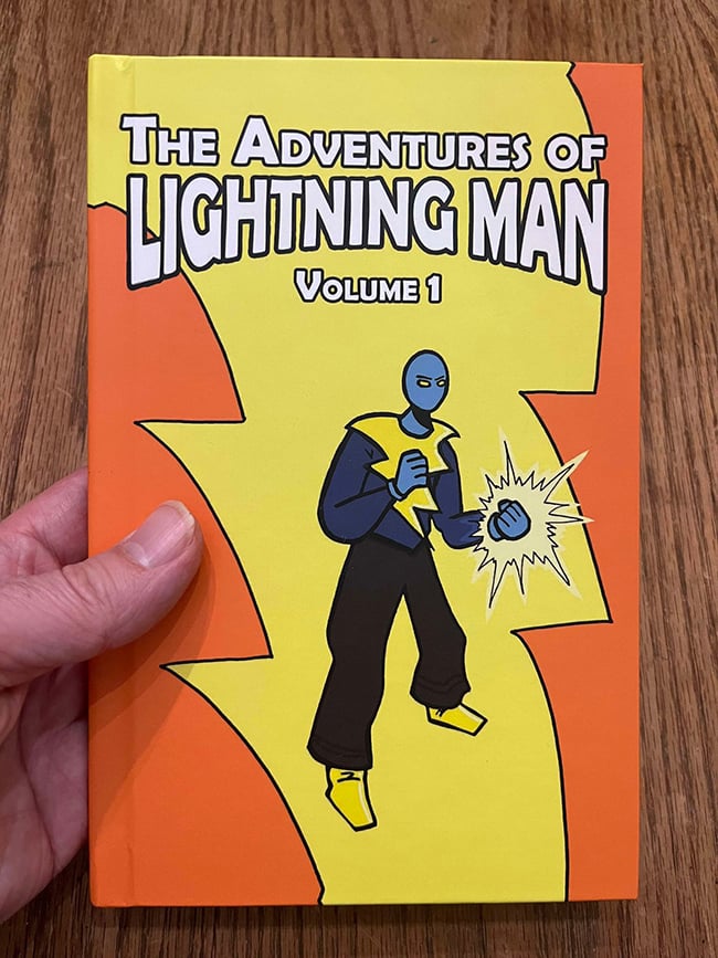 My hand holding a hardcover Lightning Man book with an orange and yellow cover