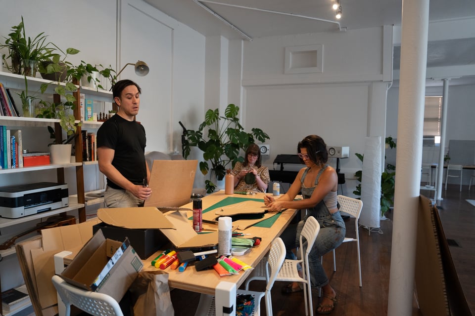 A few people seated around a table doing crafty things.