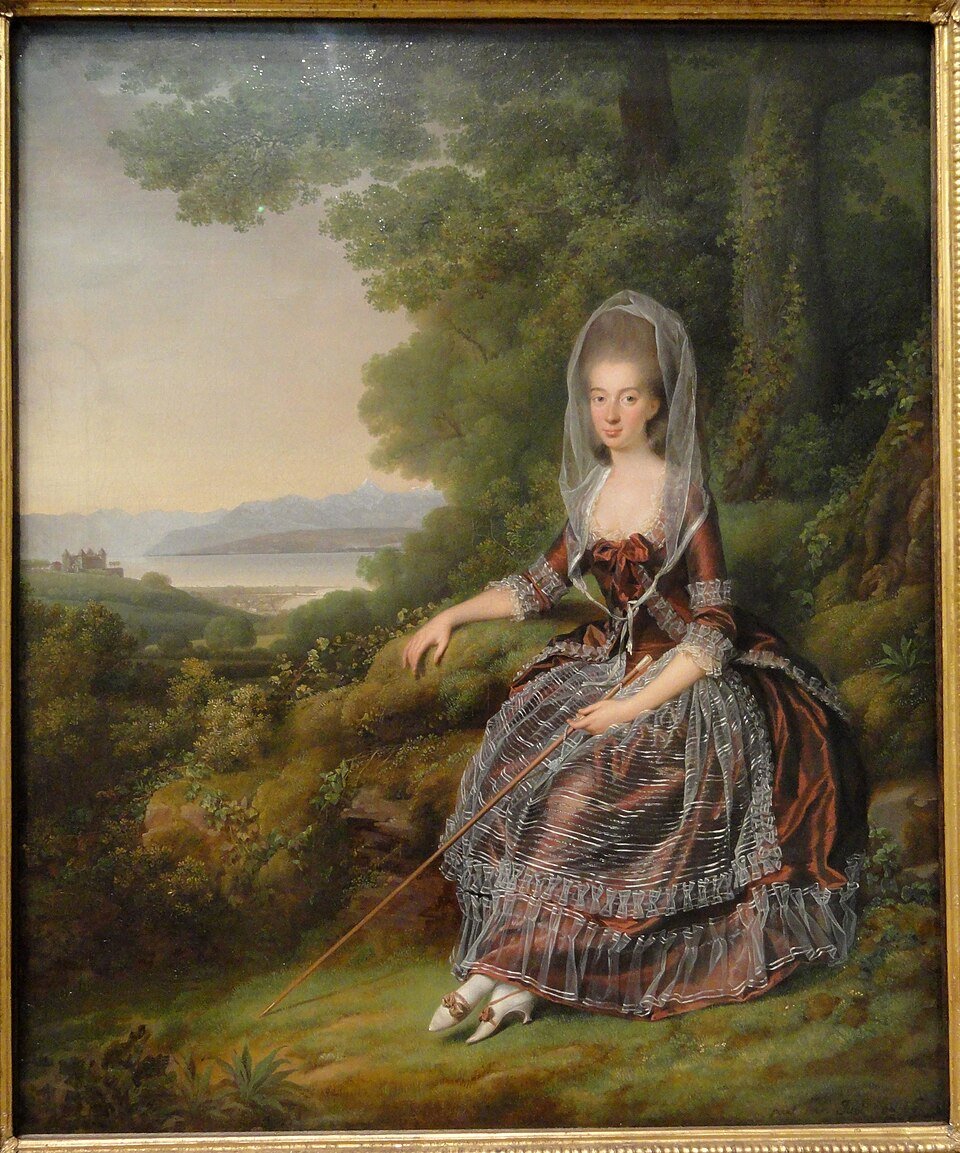 A portrait of a woman in a brown silk gown trimmed with transparent white muslin. She holds a long walking stick angled across her lap. There is a muslin kerchief draped over her hair and white shoes on her feet. She is in a picturesque landscape.