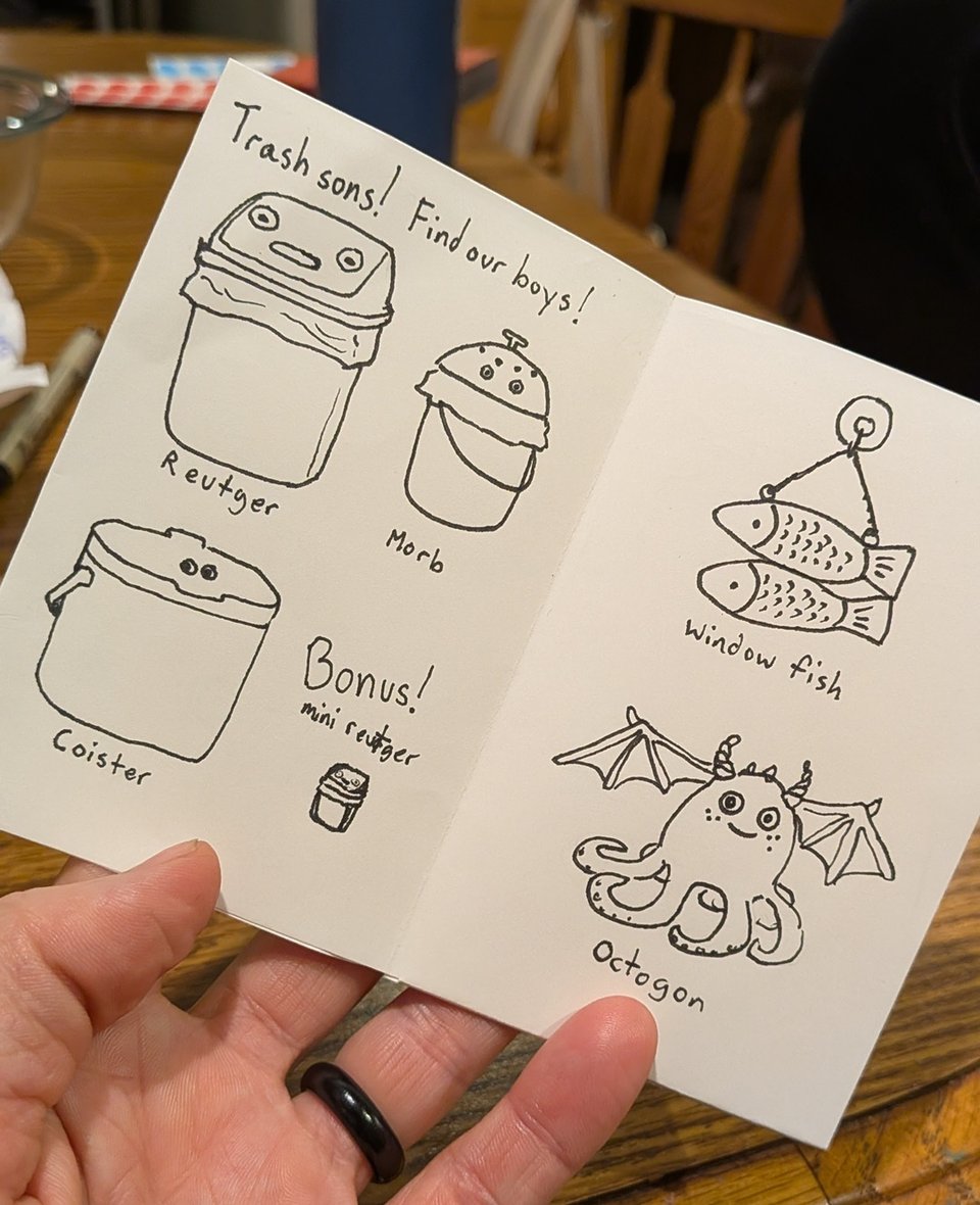a small zine, spread open to show simple black ink drawings. On one page: a trash can named Reutger, two compost bins named Morb and Coister, a mini Reutger, all with eyeballs. On the other page: two fish hanging from a chain labeled window fish, and a small octopus-like creature with bat wings and horns named Octogon