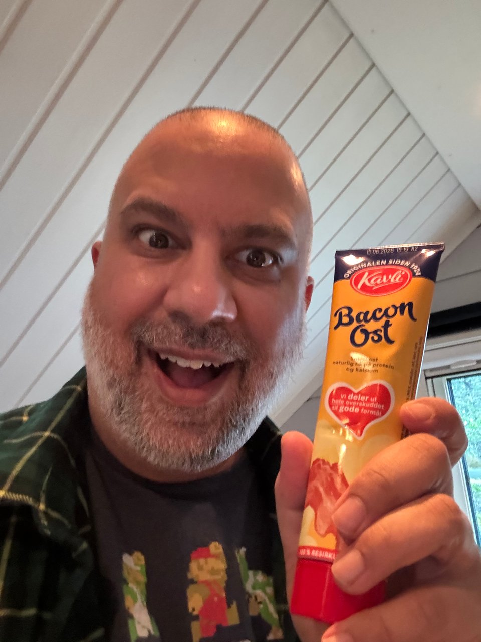 Vinny is smilling and holding up a yellow tube of Bacon Ost.