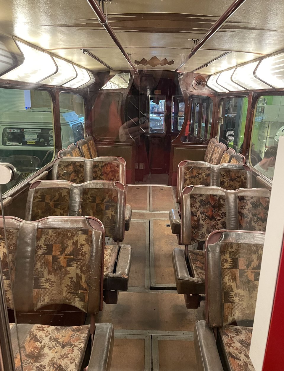 Picture of the inside of a tram, showing worn brown seating, windows in wood frames and bright lights above.