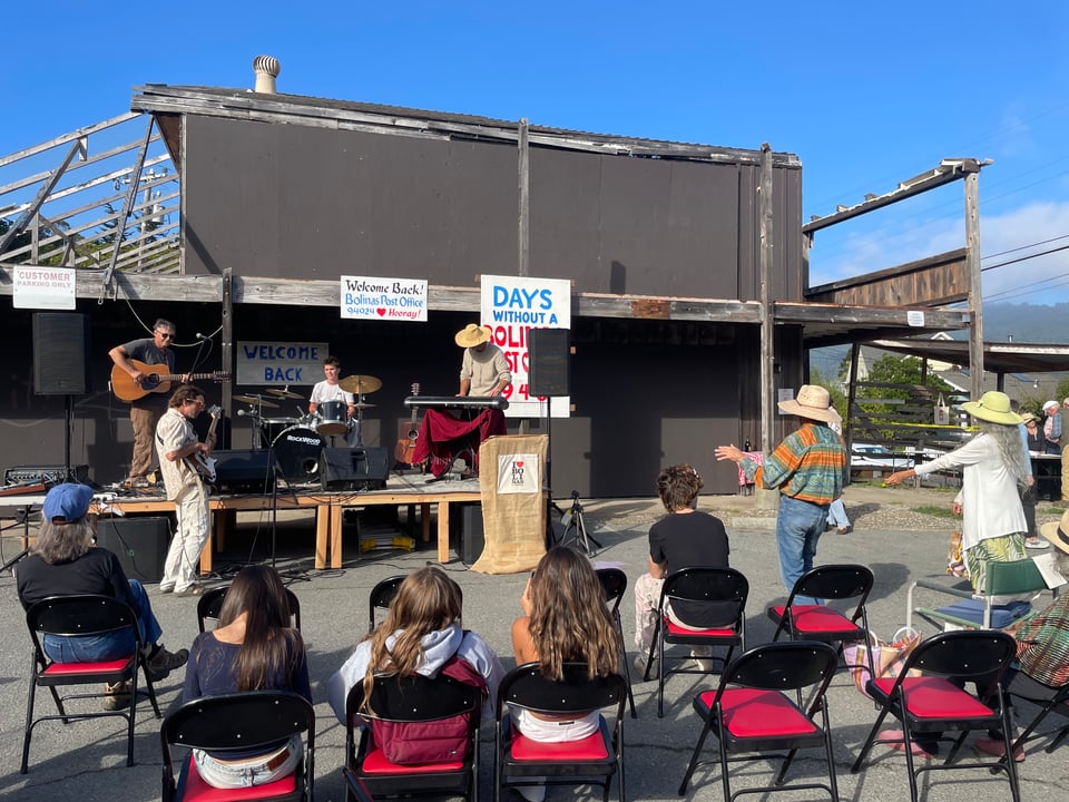 A band plays on a makeshift stage in front of an audience on folding chairs.