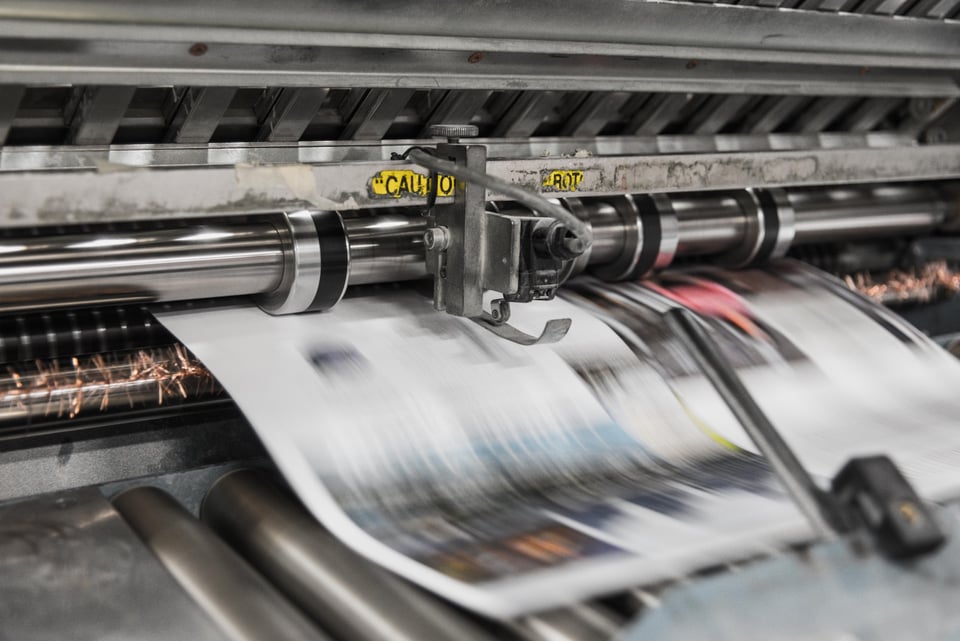 Description: image of newspaper moving through the printing press. The pages are moving so quickly that they are a blur. Photo by Bank Phrom on Unsplash.