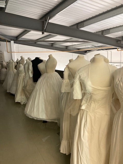 row of headless dress mannequins all dressed in white period gowns in a warehouse setting