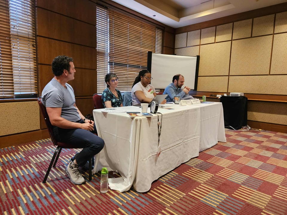 Me sitting down and speaking at a panel at Can*Con. With me are Michael Stewart, Rachel A. Rosen, and Terese Mason Pierre.