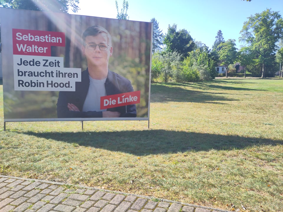Ein großes Wahlplakat steht vor einer vertrockneten Wiese. Auf dem Plakat ist ein mann abgebildet, daneben steht "Sebastian Walter. Jede Zeit braucht ihren Robin Hood."