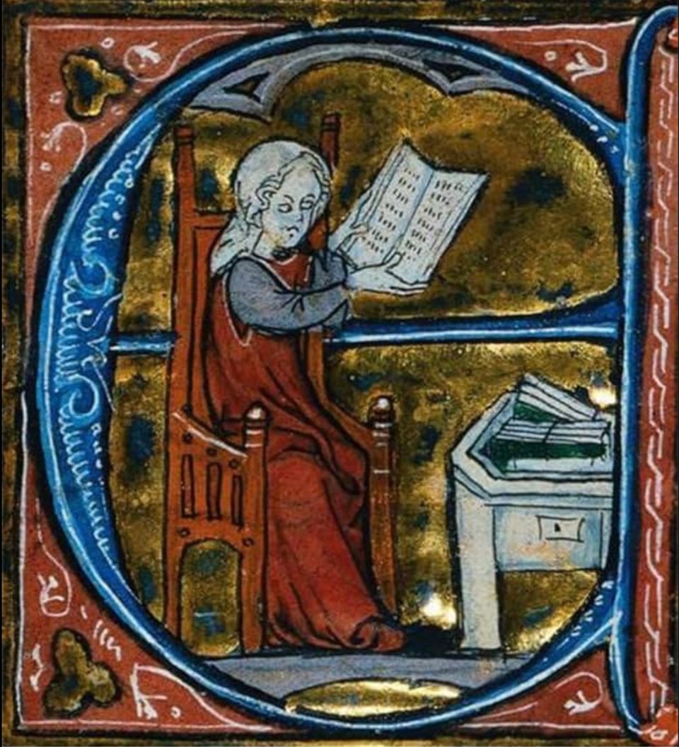 A photo of an illustration from a medieval manuscript. A dropcap capital E frames a woman, likely Marie de France, sitting in a chair. Next to her is a table with (possibly?) books on it, though it is hard to tell. She is reading a book held in her hands.