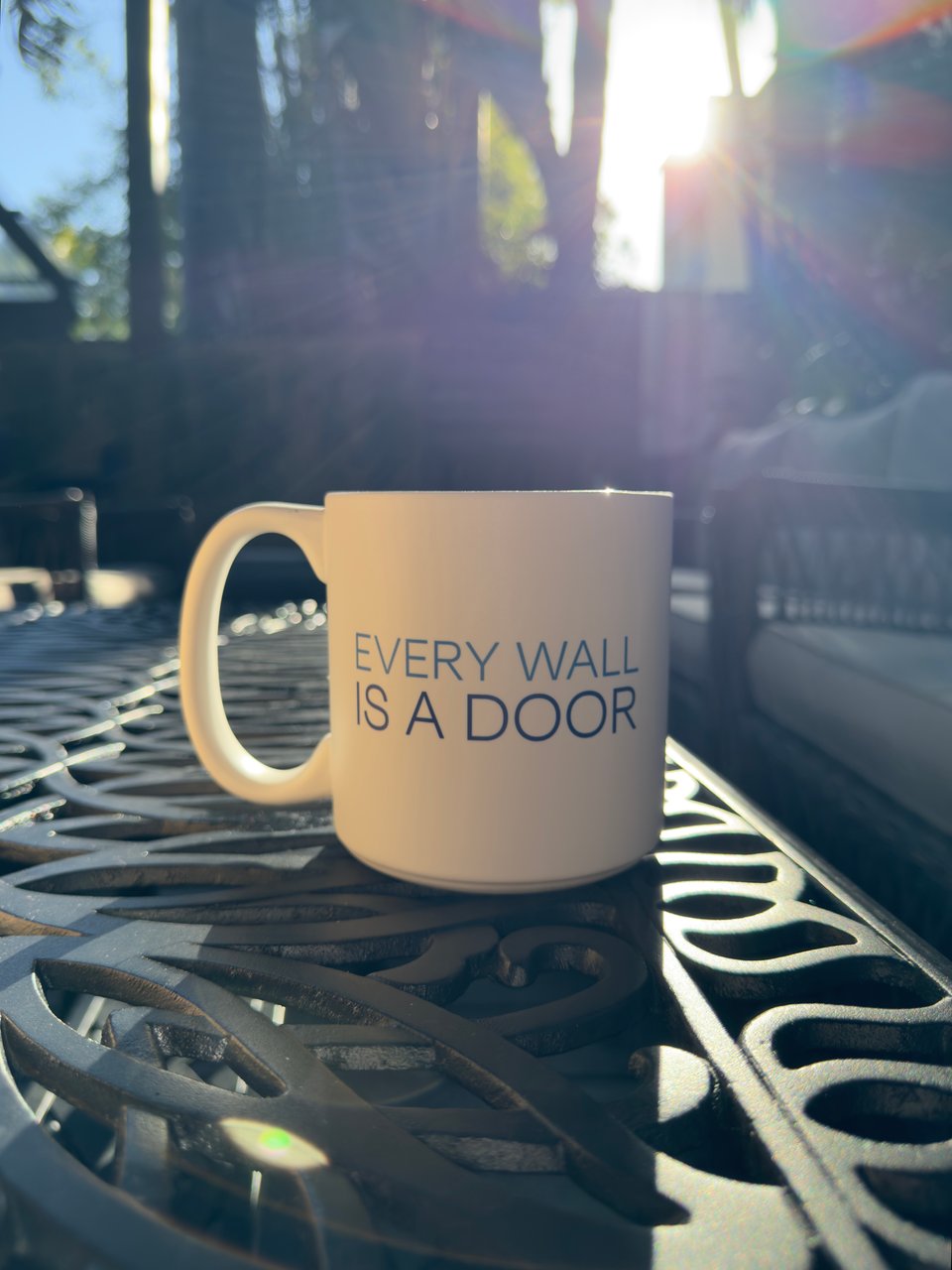 White coffee mug with the text Every Wall is a Door on a black iron coffee table outdoors