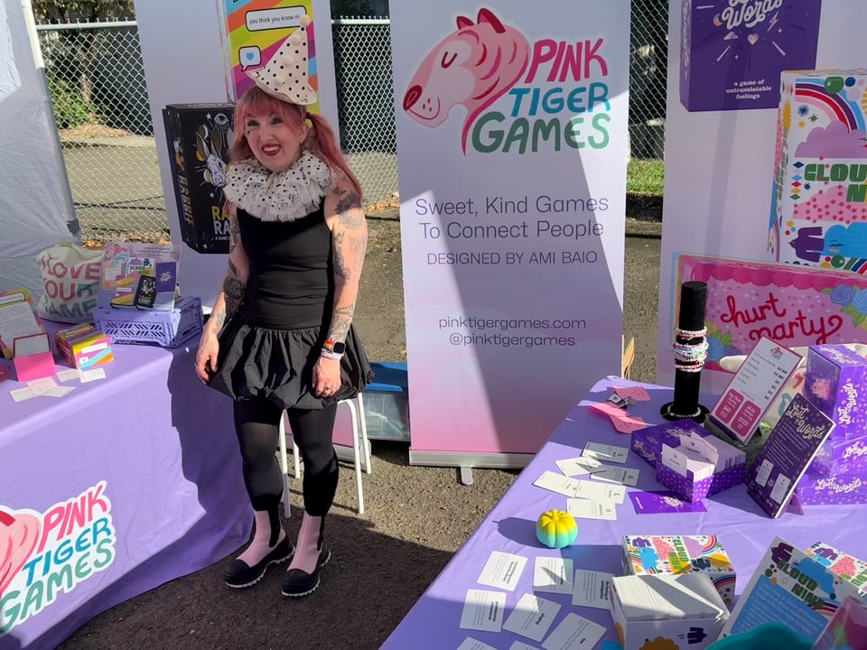 A person dressed in a cute harlequin outfit stands at a display of card games by Pink Tiger Games