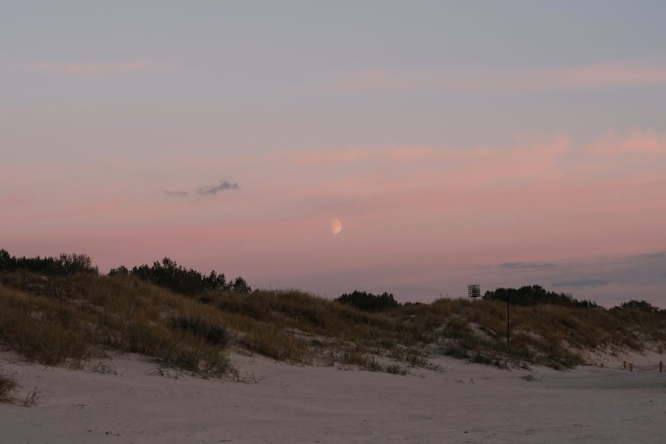 A photo of the moon over the beach during sunset.