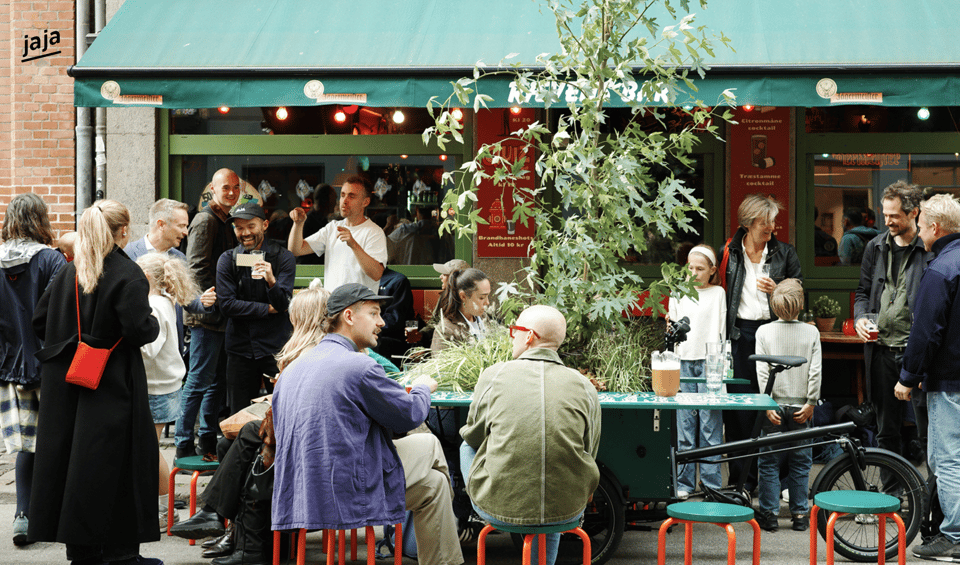 Photo of people seated outside a restaurant at the unfolded Dream Bike, which has become a table surrounded by stools, with a tree in the middle.