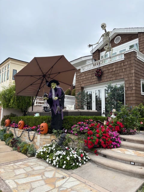A big brown house decorated with pumpkins, a grim reaper under an umbrella, and a skeleton on the roof.