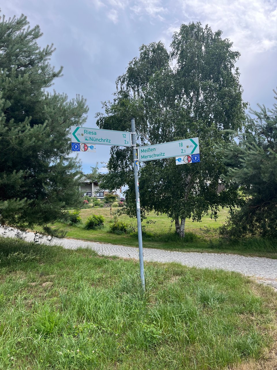 A sign showing distances to nearby towns by bike, with three logos pointing in each of the two directions. One is blue with a circle of yellow stars and the number "7" in the middle.
