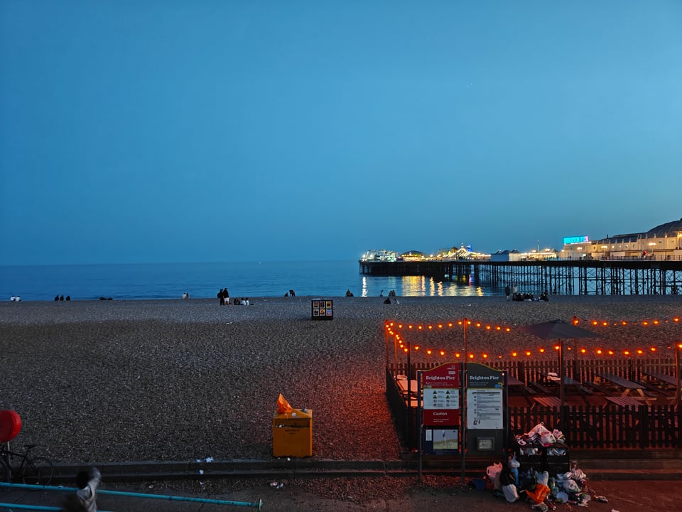 Brighton's pebble beach at night, with the pier lit up and with a deep blue sky almost exactly the same color as the sea