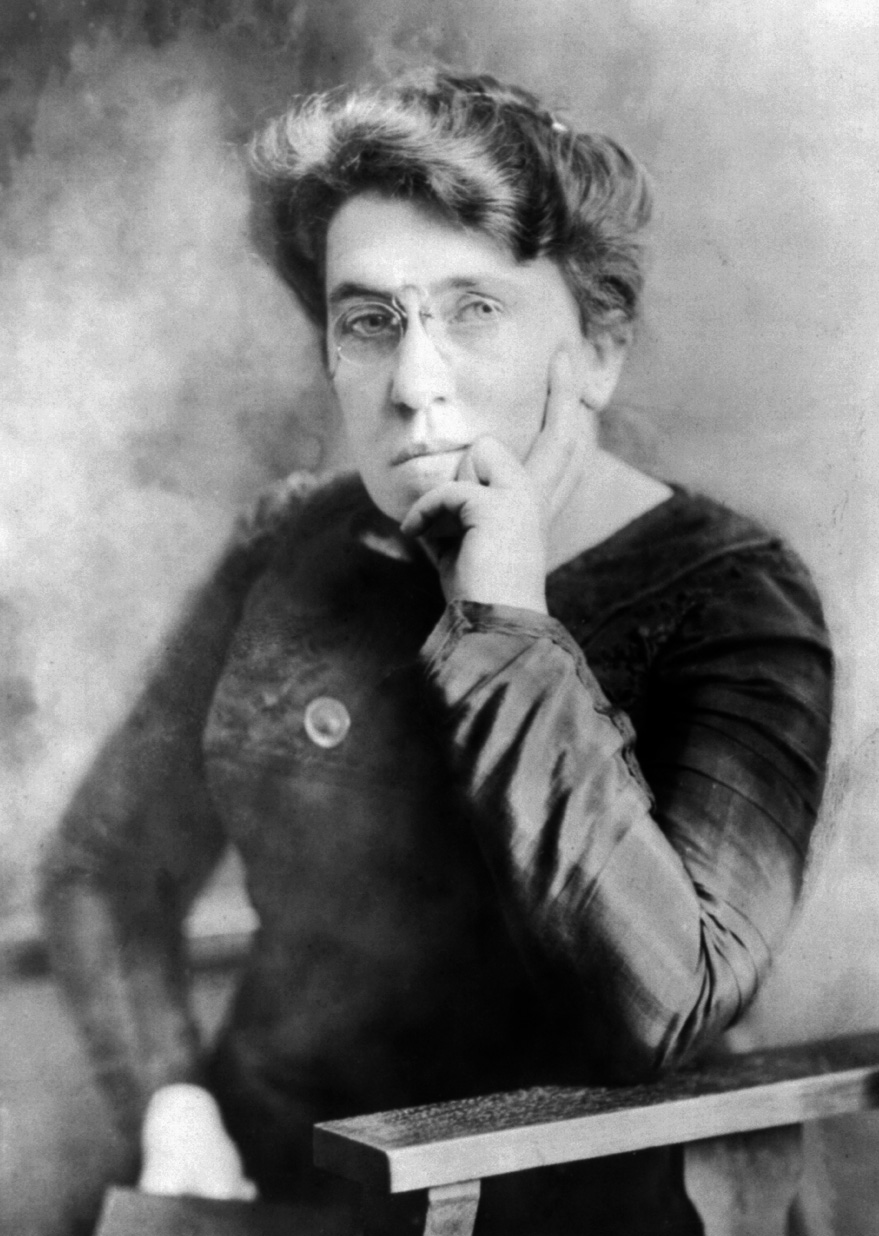 Emma Goldman, a famous anarchist activist and orator, sits staring judgmentally at the camera through her nose-pinch eyeglasses, one hand thoughtfully supporting her chin.