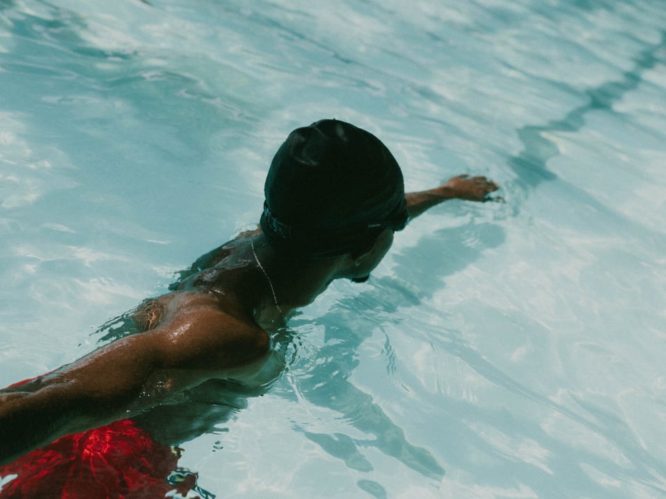 Peter in the water, clad in a cap and goggles, about to push off into a stroke.