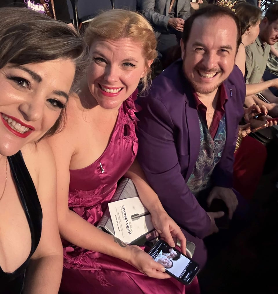 Natania, Cass, and Marshall sitting in the audience for the Hugo Awards, smiling at the camera.