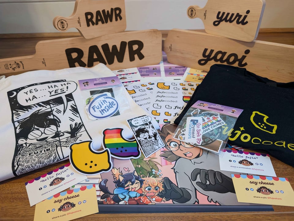 An array of FujoCoded merchandise on a wooden floor. In the back of the array are four fujoboards, with a chibi version perching on top of the two larger hime versions, all standing on end so the inscribed text is visible. Two say “rawr” and the other two say “yuri” and “yaoi.” Underneath the other merchandise are several sheets of FujoCoded logo stickers and a print of Boba-tan watching Git and GitHub squabble. On the left and right of the pile are two folded tee shirts. On top of the tee shirts are sticker packs and large FujoCoded lemon logo stickers. At the front of the array are four packing cards with FujoCoded branding that say either “hello fujin” or “say cheese.”<br/>