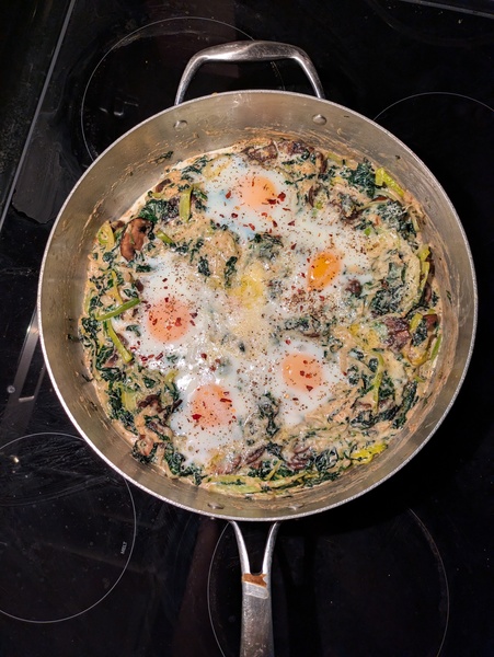 a high-walled pan containing baked eggs, greens, and mushrooms in a creamy sauce