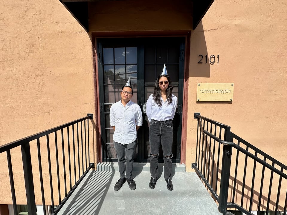 Two people wearing silver birthday hats, white button downs, black pants, and black shoes.