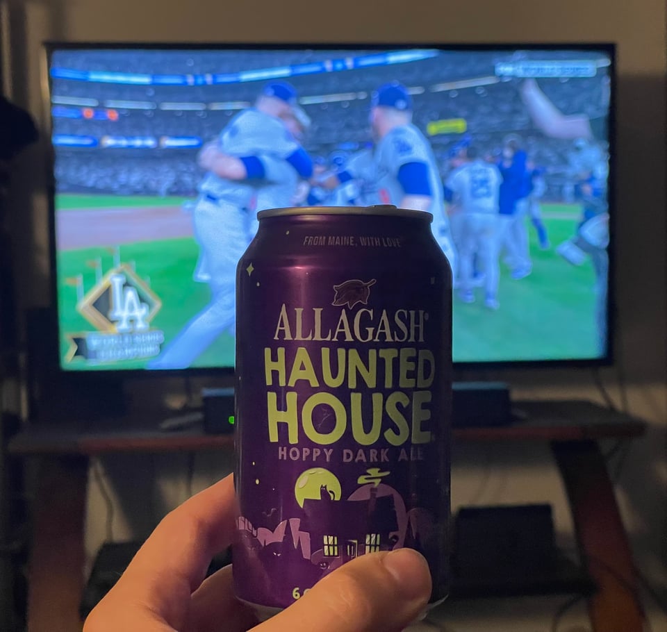 A beer called Haunted House held up to cheers a television where members of the Dodgers baseball team are hugging one another