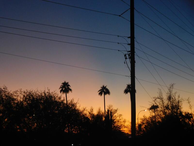 A utility pole and plam trees silhoutted against a colorful sunset.