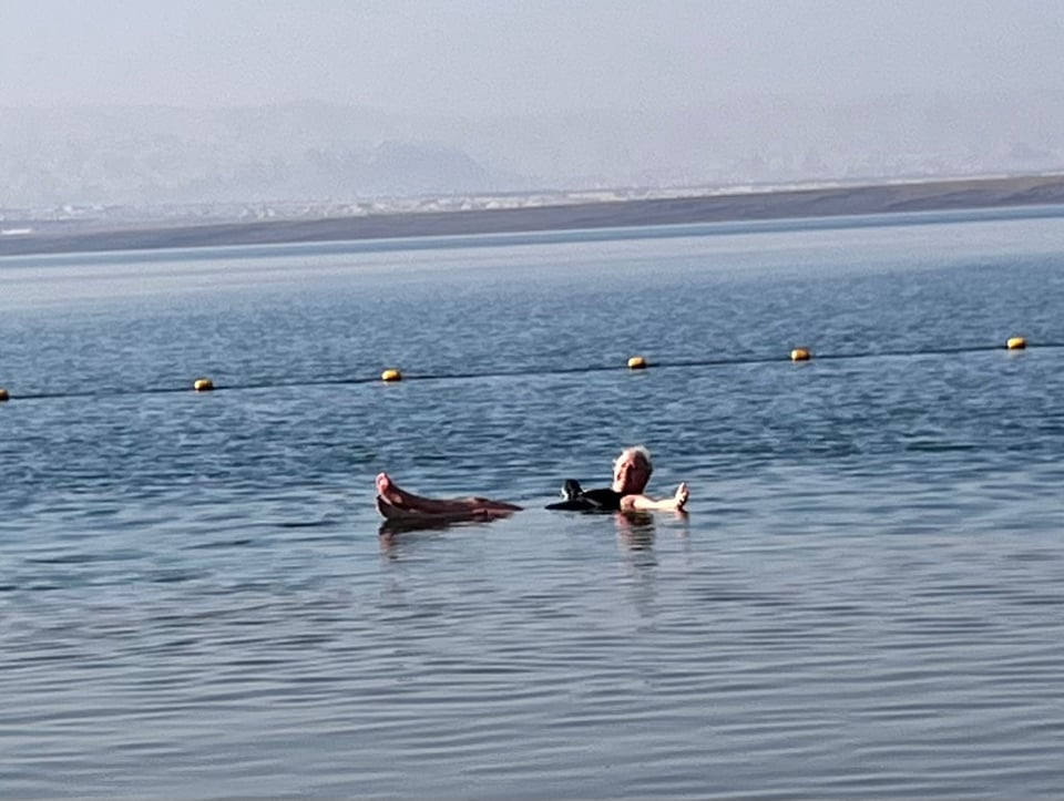 a smiling woman who is lying down seemingly on top of water, with her legs crossed and arms outstretched