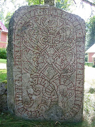 A stone upright that looks like a tombstone, with curving designs including strings of runes.