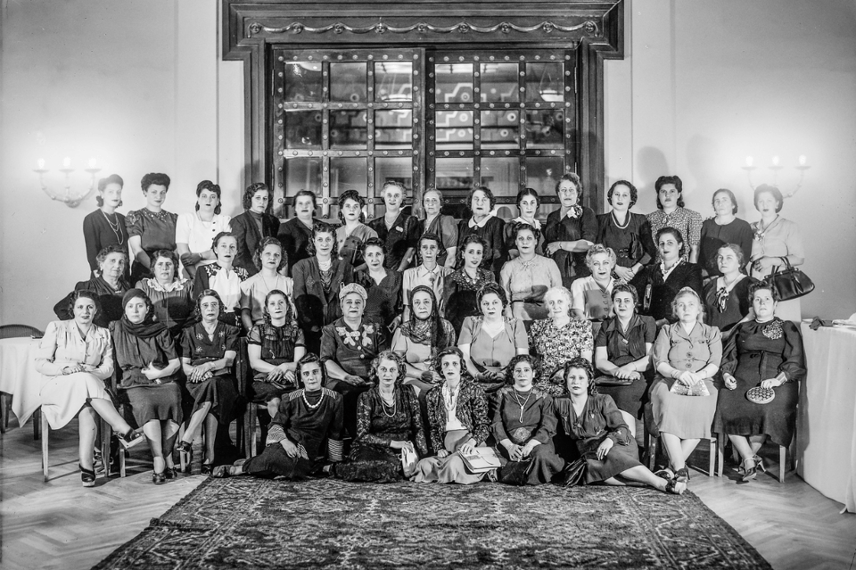 Three rows of women (about 12 women per row) posing for a photograph in front of a large window