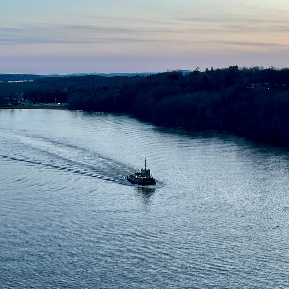 an intrepid tugboat makes its way up the Hudson river at dusk