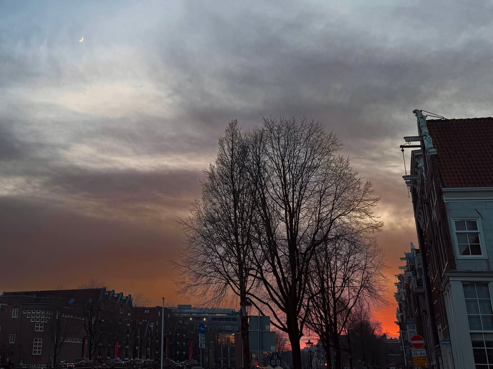 A deep orange sunset on the horizon with a small crescent moon in the top left corner of the photo.