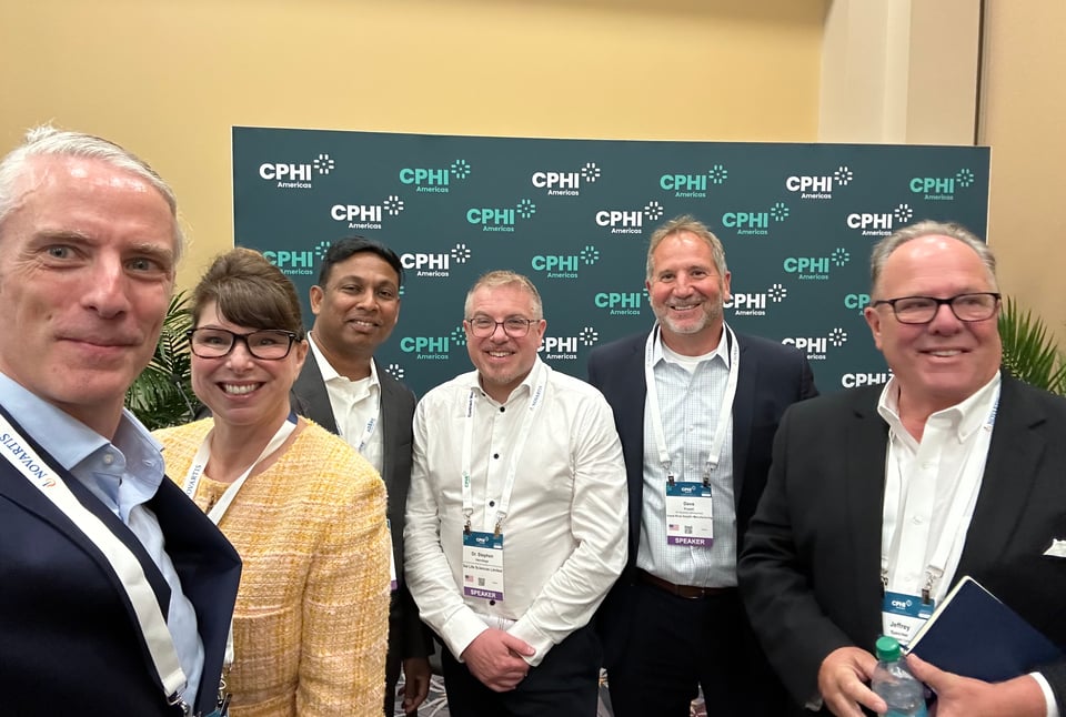 Photo of 6 people standing in front of a backdrop that reads CPHI Americas. They have just finished a ~90-minute panel at a conference, but are somehow smiling Photo of 6 people standing in front of a backdrop that reads CPHI Americas. They have just finished an 85-minute panel at a conference, but are somehow smiling.