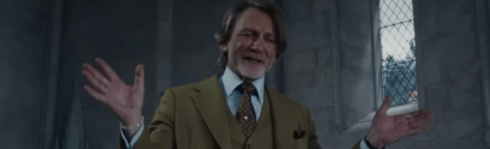 A still from Wake Up Dead Man: a white man in a fancy suit and floppy, greying hair looks positively gleeful.