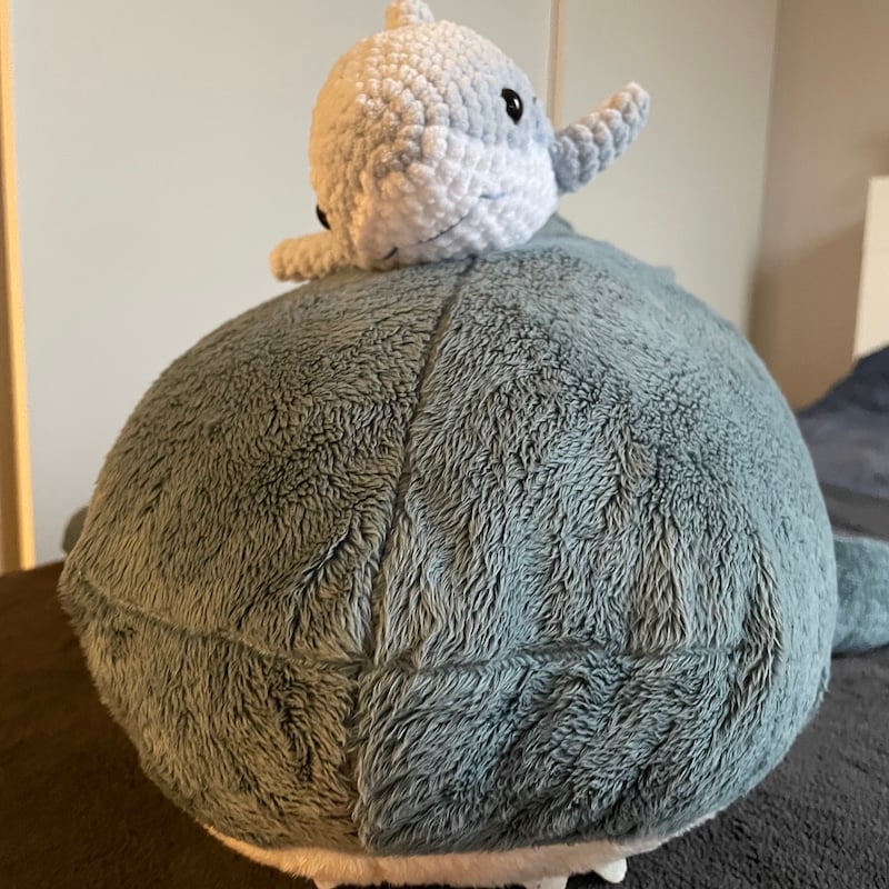 An image of one small knitted shark on top of a large plush shark.