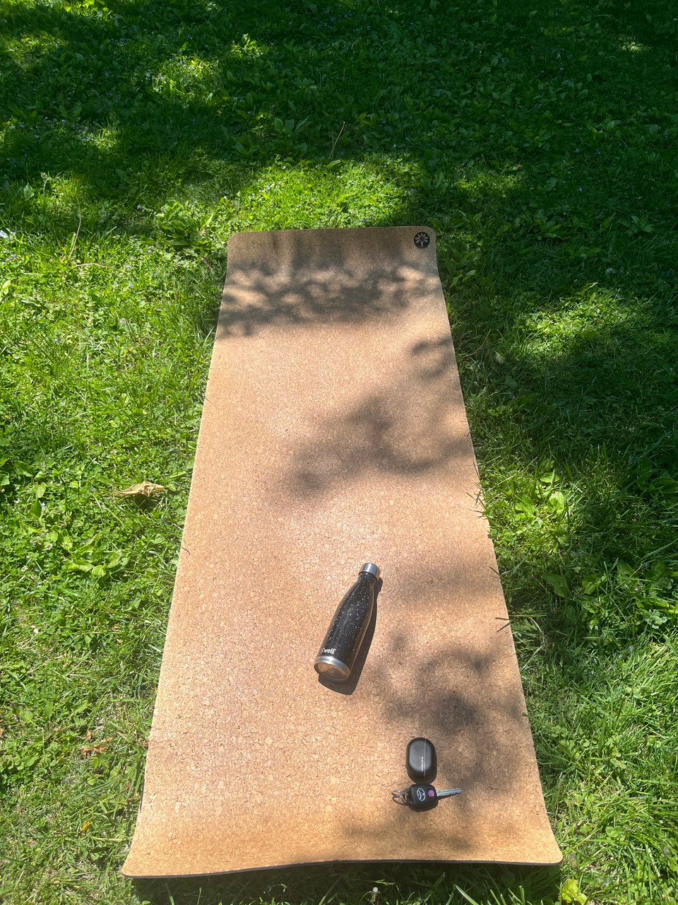 an exercise mat, water bottle, and keys in dappled sun on park grass
