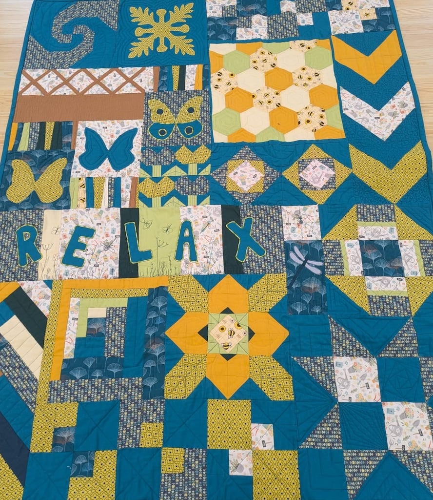 A blue, green and yellow patchwork quilt incorporating leaves, butterflies, and the word "relax"