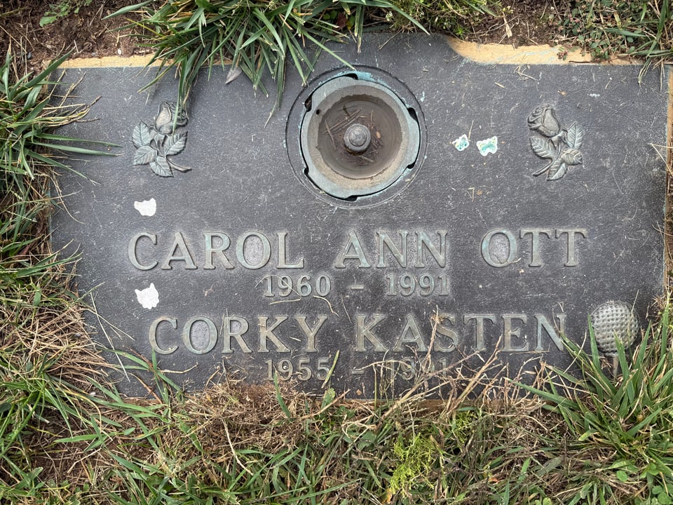 photo of grave marker surrounded by grass. It reads
CAROL ANN OTT
1960-1991
CORKY KATEN
1955-1991
and there's a golfball on a tee carved in relief beside Corky's name. There are also some small butterfly stickers attached to the marker, faded in time.