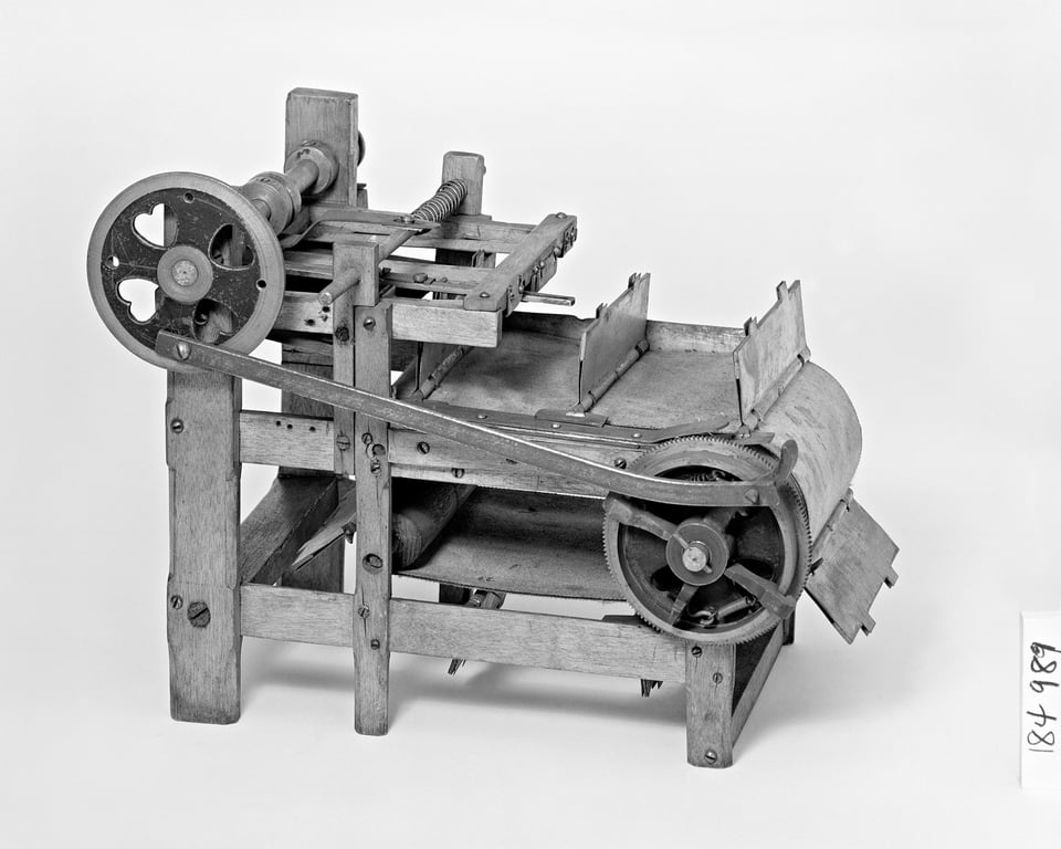 A black and white photo of a patent model of a book sewing machine, with gears and a conveyor belt, made out of wood and metal.