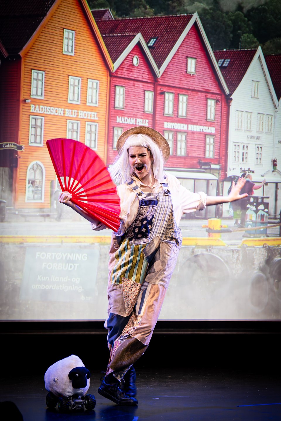 booth as a bedraggled farmer waving a beautiful fan, dancing, while a tiny sheep stands beside them