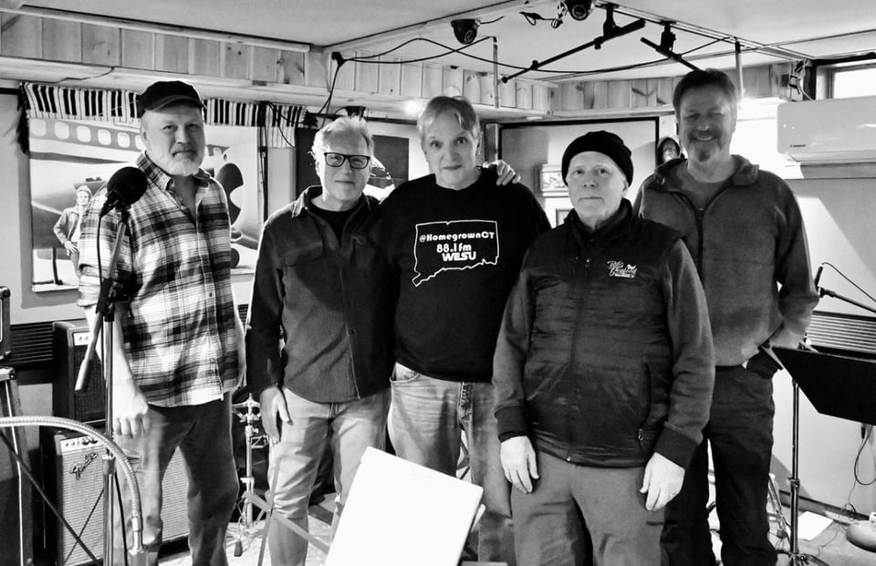 Five people stand together in a recording studio in a black and white photo.
