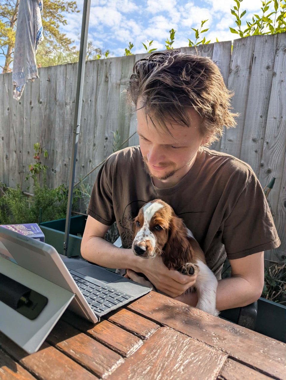Me, sat in the garden at my laptop, a puppy in my arms.