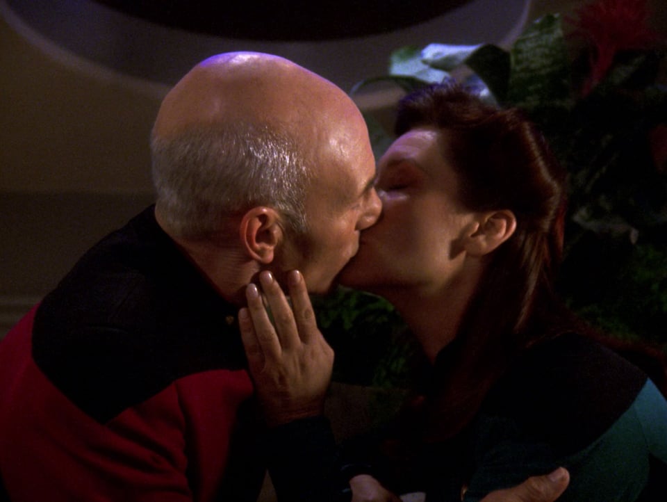 Captain Picard and Commander Darren, sharing a romantic kiss. Her hand is on his face, his hand is holding her shoulder. Their eyes are closed.