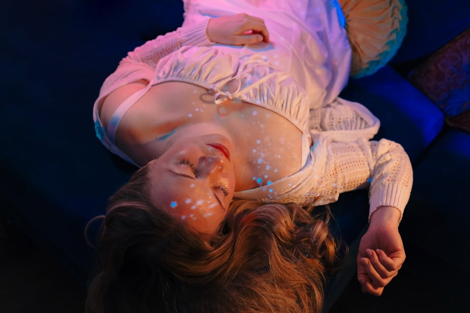 A photograph of Emily lying down in a white dress. Projections of little stars are scattered across her.
