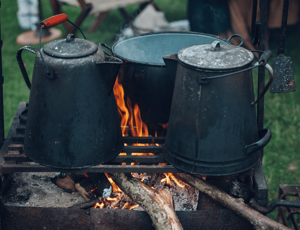 A campfire with a grill on top, holding three coffee pots.